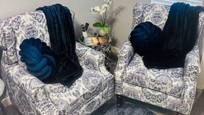 Due poltrone con motivi decorativi e cuscini scuri, un tavolino con un vaso di fiori bianchi e decorazioni a parete.