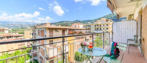 A balcony with a table and chairs, overlooking a residential area with buildings and greenery.