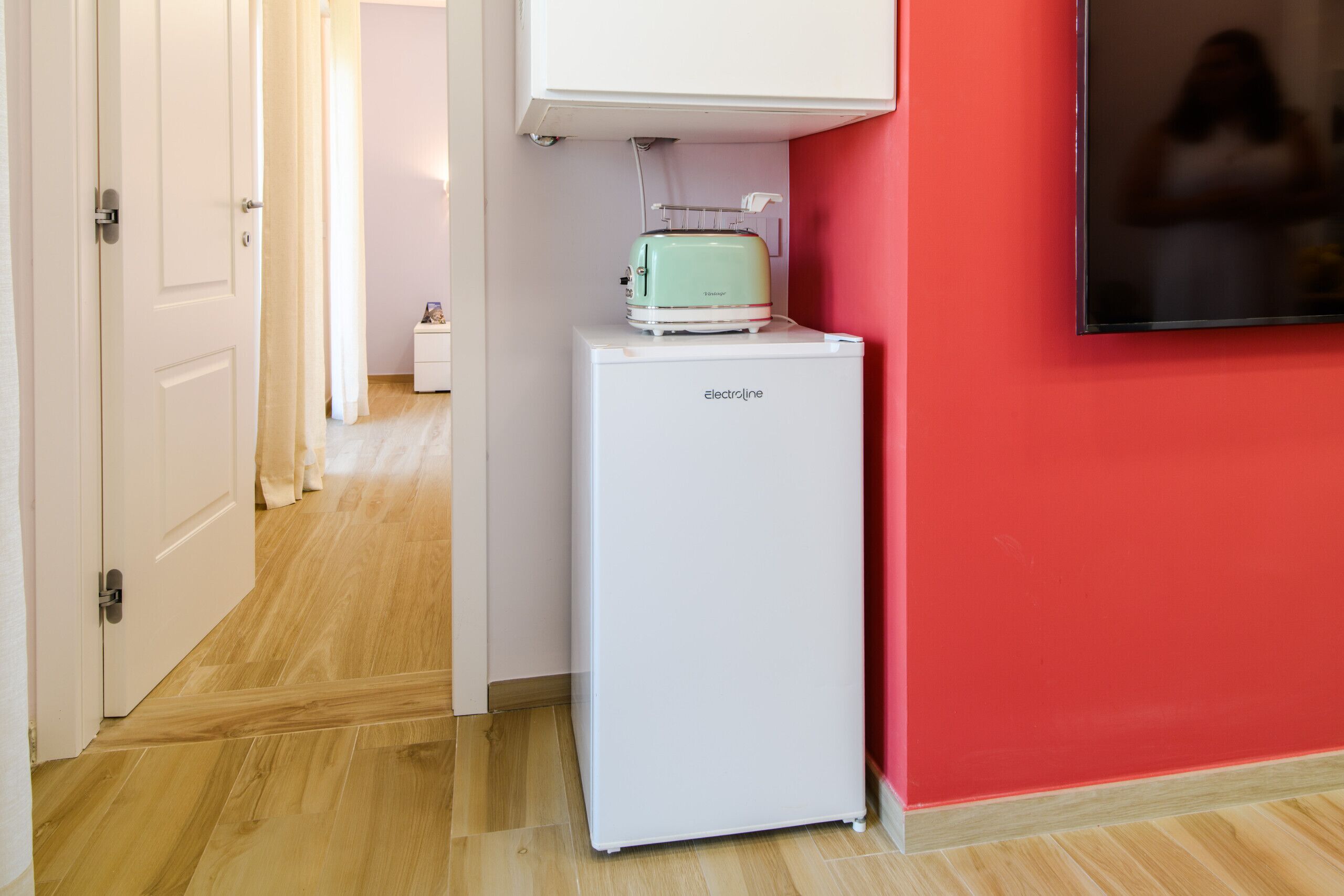A compact room with a white refrigerator, a small table with a toaster, and a red wall.