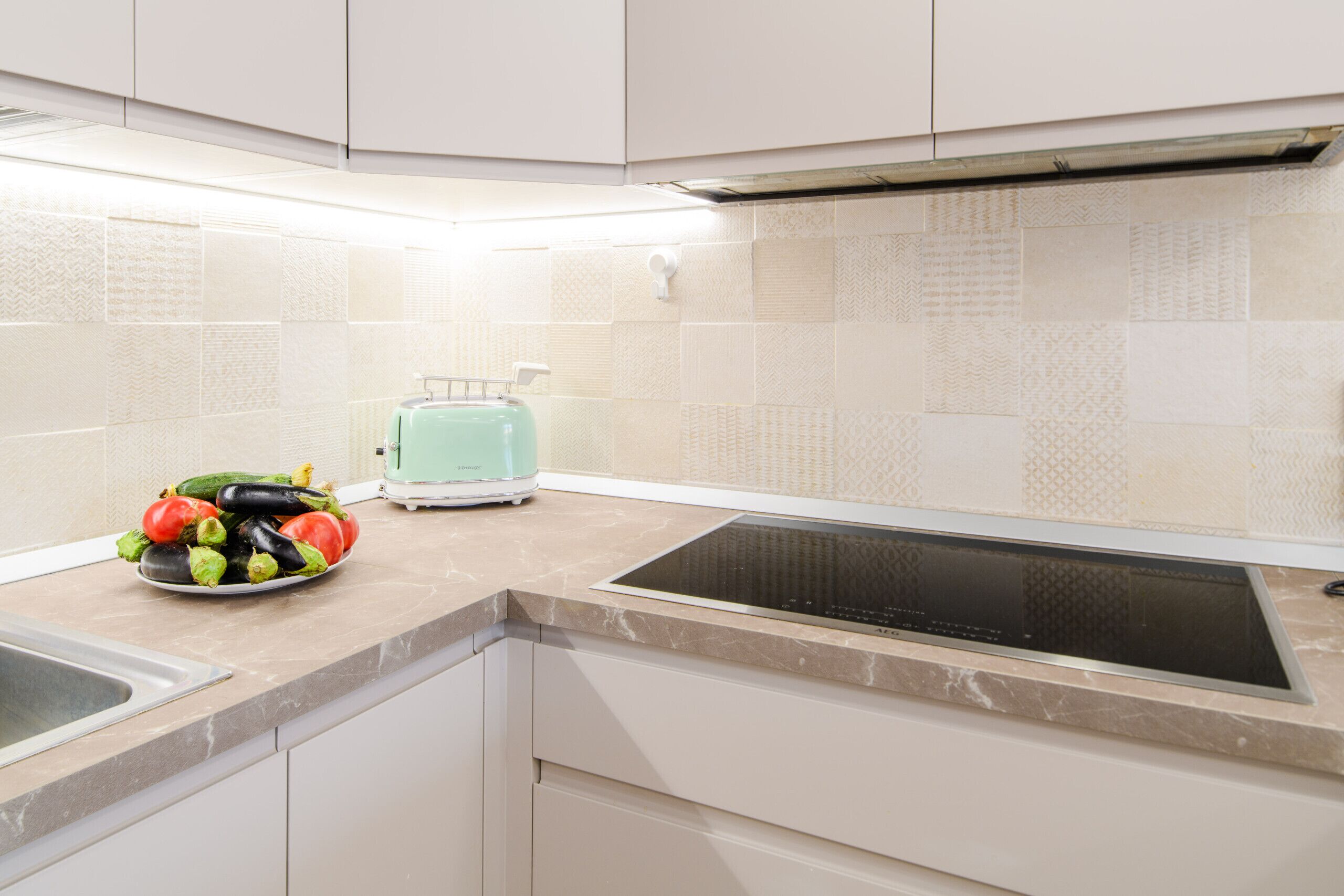Una cocina moderna con estufa integrada, un tostador y un bol de verduras sobre la encimera.