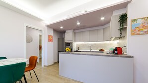 A modern kitchen with a central island, white cabinets, and a dining area with a green table and orange chairs. - Domus Sirenum - Partenope (Sorrento)
