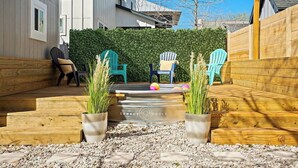 A backyard with a wooden deck, two Adirondack chairs, a small pool, and potted plants.