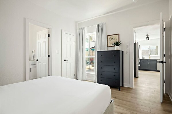 A bedroom with a bed, a dresser, and a view to the kitchen.