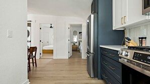 A modern kitchen with a refrigerator, oven, and microwave. There is a dining area with a chair and a table.