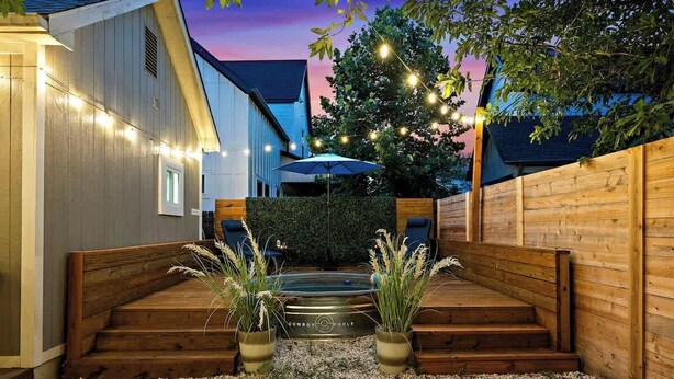 A wooden deck with steps leading to a seating area, surrounded by a wooden fence and a hedge.
