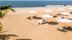 Una playa con sombrillas blancas y sillas reclinables.