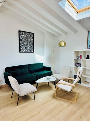 Uma sala de estar moderna com um sofá verde, duas poltronas, uma mesa de centro, um abajur e uma estante de livros.