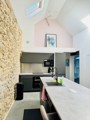 A modern kitchen with a stone wall, a large island, and a ceiling light. - Renovated family loft 120 m2 3 bedrooms Marseille 8e (Marseille)