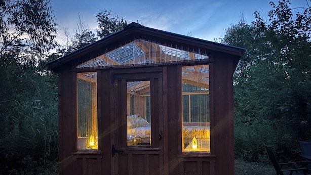 Eine Holzhütte mit einem verglasten Schlafbereich, einer Tür und zwei erleuchteten Fenstern.