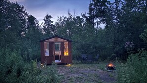 Eine kleine Holzhütte mit einem Feuerkorb im Vordergrund, umgeben von dichtem Grün.