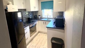 A compact kitchen with white cabinets, a black refrigerator, and a window with blue curtains.