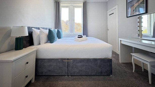 A modern hotel room with a large bed, a desk, and a window with curtains.