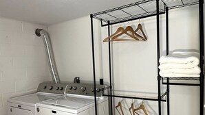 Un espace buanderie comprenant un lave-linge, un sèche-linge et un étendoir métallique muni de cintres et de serviettes pliées.