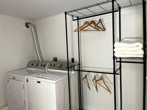 Ein Waschraum mit einer Waschmaschine, einem Trockner und einem Wäscheständer mit Kleiderbügeln und gefalteten Handtüchern.