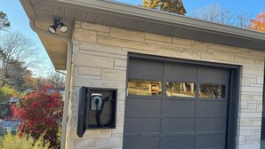 Un garage doté d’une borne de recharge, une façade en pierre et une vue sur les environs.