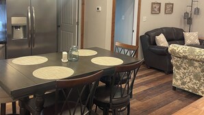 Eine moderne Küche mit einem Edelstahlkühlschrank, einem Esstisch mit Platzsets und einem schwarzen Ledersofa im Wohnbereich.