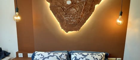 A bedroom with a bed, two bedside tables, a wall-mounted light fixture, and a wall art piece.