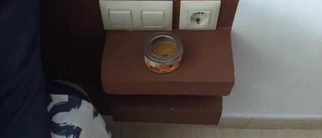 A small bedside table with a lamp, a power outlet, and a small container.