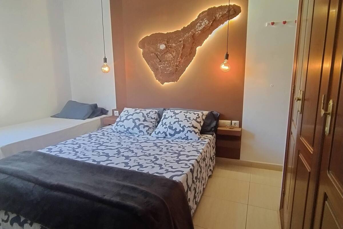 A bedroom with a bed, a nightstand, a wall-mounted light fixture, and a wardrobe.