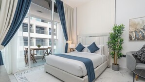 A modern hotel room with a large bed, a potted plant, a sofa, and a balcony with a table and chairs. - Vogue | Opalz by Danube Arjan near Science park (Dubai)