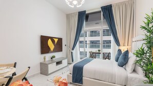 A modern bedroom with a bed, a dining table, and a view of a building through large windows. - Vogue | Opalz by Danube Arjan near Science park (Dubai)