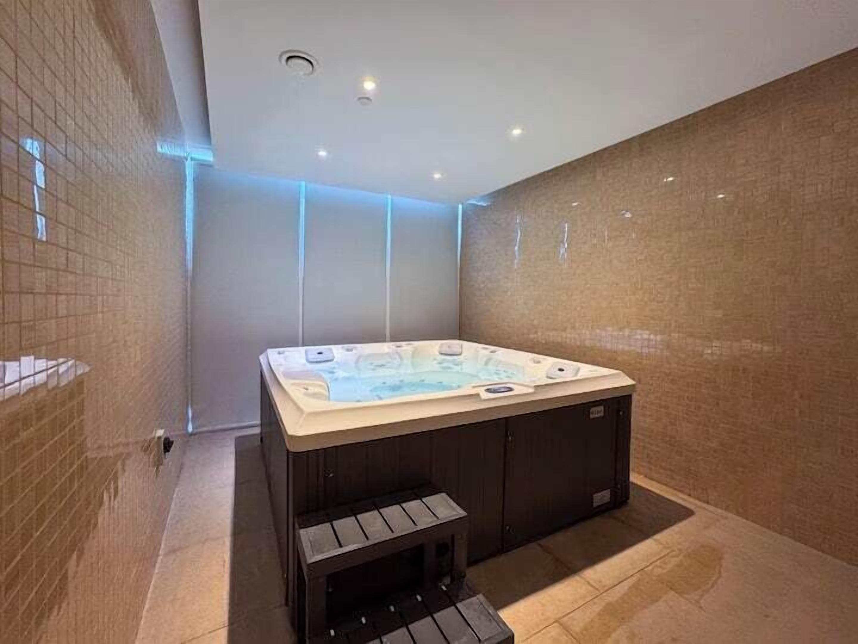 A modern bathroom with a hot tub, tiled walls, and recessed lighting.