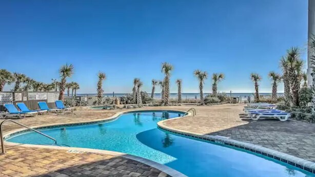 A swimming pool with blue water, surrounded by lounge chairs and palm trees, with a clear view of the ocean in the background. - Destination Ocean, Unobstructed Oceanfront Suite with a King Bed (Myrtle Beach)