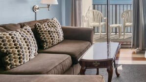 A living room with a sofa, a lamp, and a view of the balcony with chairs. - Destination Ocean, Unobstructed Oceanfront Suite with a King Bed (Myrtle Beach)