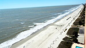 A beach with a long stretch of sand, a few people, and a pier in the distance. - Destination Ocean, Unobstructed Oceanfront Suite with a King Bed (Myrtle Beach)