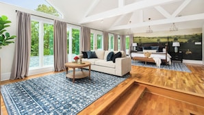 A spacious living room with a large window, a sofa, a coffee table, and a painting on the wall. - Bourbon Trail Estate, Golf Sim, SpeakEZ, Sleeps 14 (Frankfort)