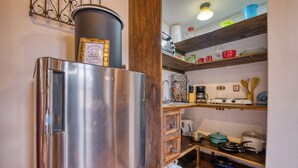 Una cocina compacta con un refrigerador de acero inoxidable, repisas de madera con diversos utensilios de cocina, y una pequeña encimera con una cafetera y cubiertos.