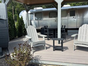 Ein Außenbereich mit einer Terrasse, Adirondack-Stühlen, einem Tisch und einer überdachten Sitzgelegenheit.