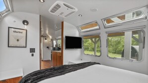 Interior moderno de autocaravana con cama, kitchenette y televisor montado.