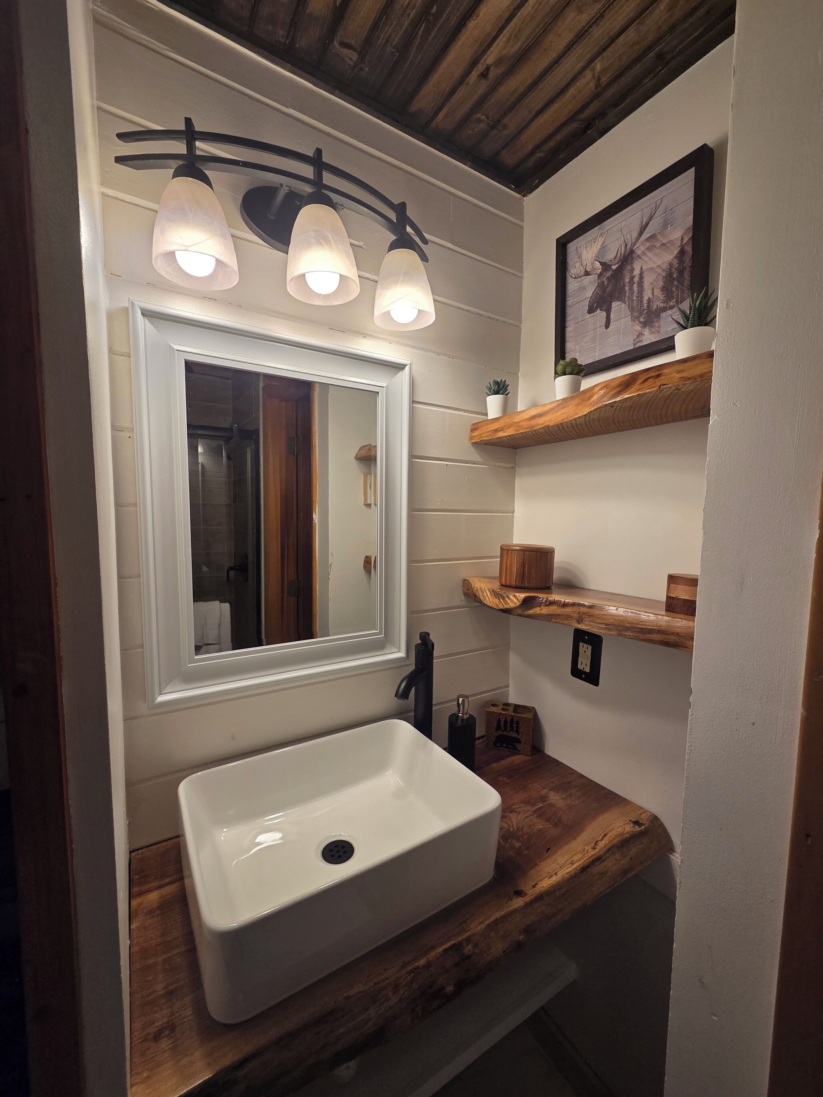 A bathroom with a white sink, a mirror with a wooden frame, and a wooden shelf above the sink.