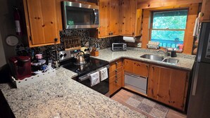 Une cuisine dotée de plans de travail en granit, de meubles en bois, d’une cuisinière en acier inoxydable, d’un four à micro-ondes, d’un grille-pain et d’une fenêtre donnant sur un paysage verdoyant.