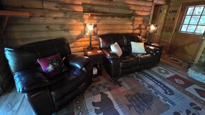 L’intérieur d’une cabane en rondins, avec un ensemble de canapés en cuir, deux lampadaires et un tapis à motifs.