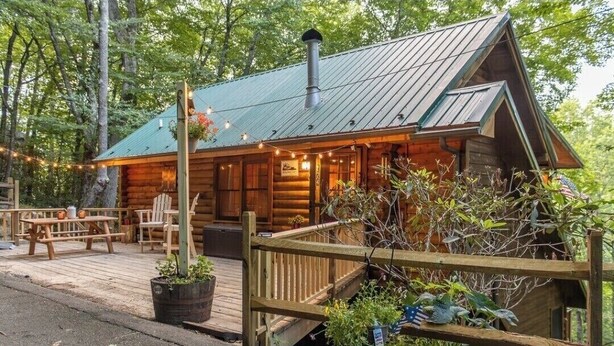 Une cabane rustique en rondins de bois, dotée d’un toit en métal, d’une terrasse en bois et d’un espace de détente extérieur.