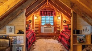 Une chambre mansardée chaleureuse avec un plafond en pente, deux lits avec une literie à carreaux rouges et noirs, un tapis en fourrure et une fenêtre offrant une belle vue.