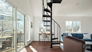 A modern interior with a spiral staircase, a glass wall, a sofa, and a desk. - E ATX Tree House | Deck | Fire Pit | BBQ | Parking (Austin)