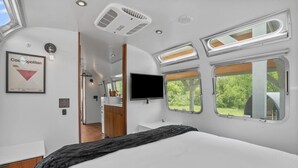 Ein modernes Wohnmobil-Interieur mit einem Bett, Dachfenstern, einem angebauten Fernseher und einer Küchenzeile.