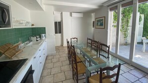 Cocina moderna con armarios blancos, una mesa de comedor de vidrio y sillas de madera. Se ve follaje a través de la puerta corrediza de vidrio.