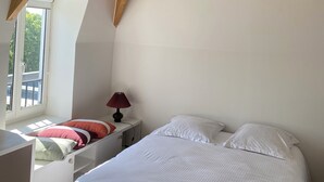Un dormitorio con techo inclinado, una cama, una mesita de noche con una lámpara y una ventana con vistas al exterior.