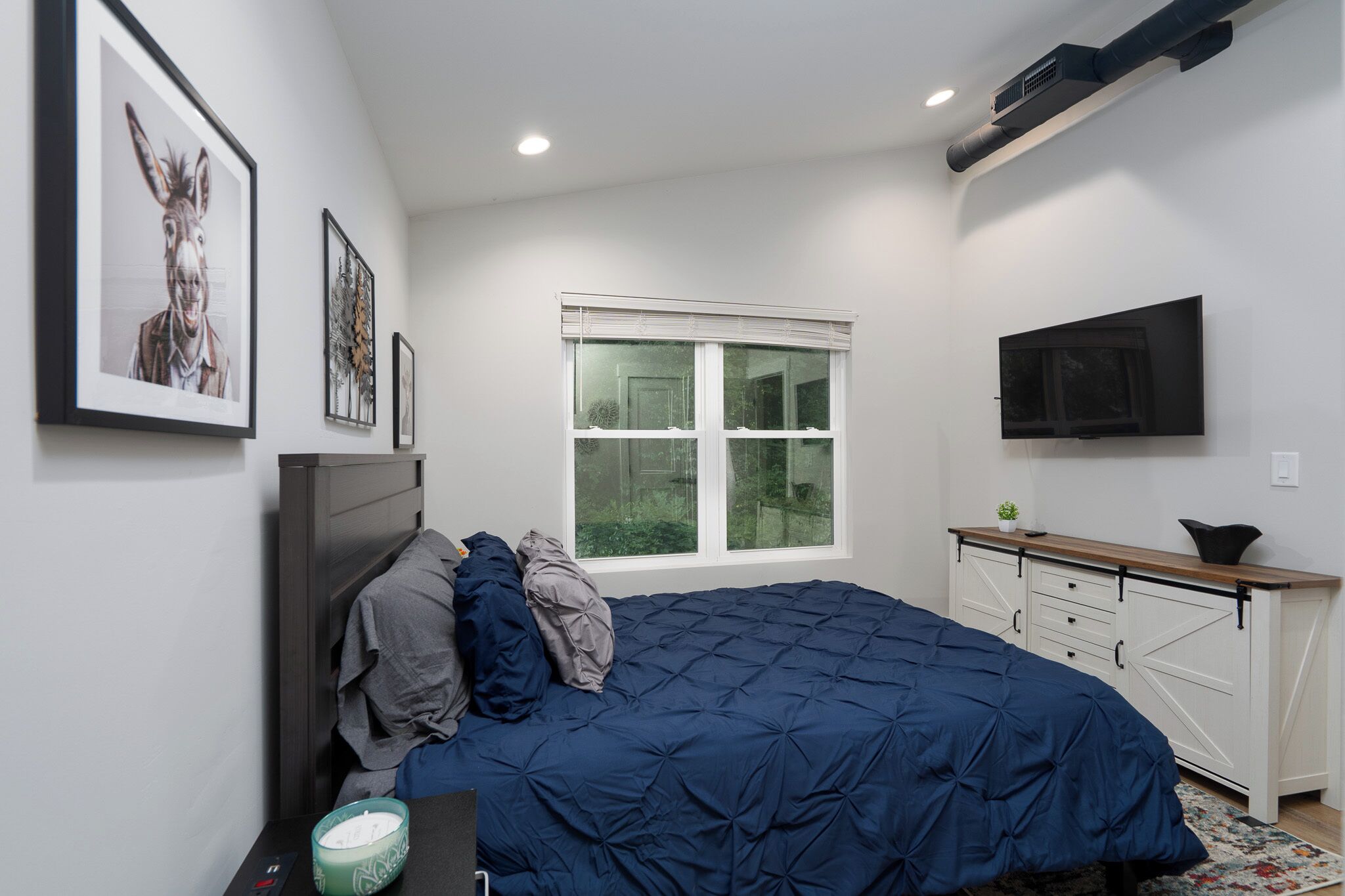 A bedroom with a large bed, a window, a TV, and a dresser.