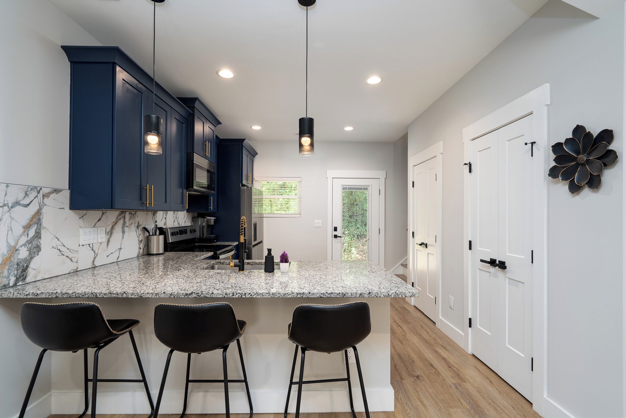 A modern kitchen with dark blue cabinets, a granite countertop, and three black bar stools.