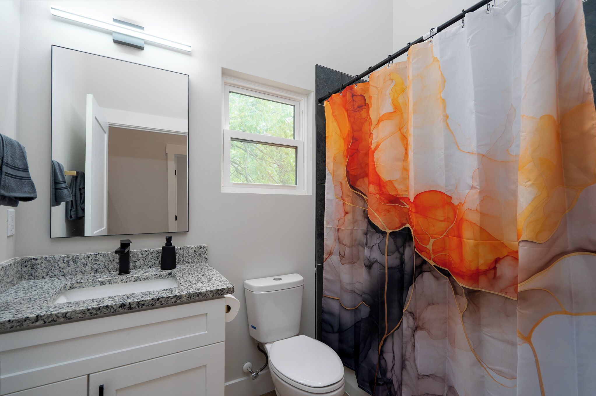 A bathroom with a granite countertop, a white toilet, and a shower curtain with an abstract design.