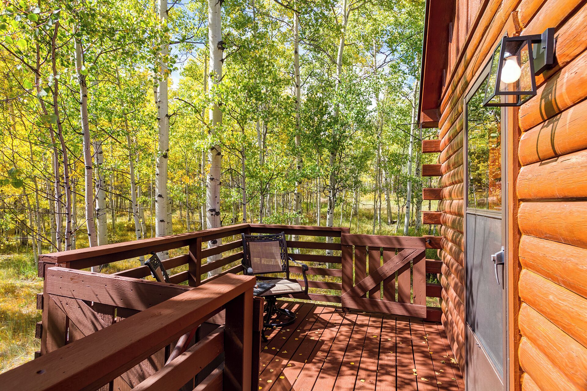 Una terraza de madera con un banco y una mesa, rodeada de un bosque.