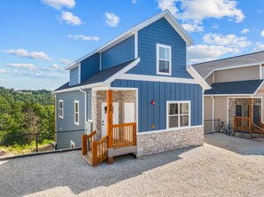 A two-story house with a stone foundation, a wooden deck, and a clear view of the surrounding landscape. - Modern Family Lodge 1 Mi to Silver Dollar City, Indoor Pool, Hot Tub, Arcade, EV (Branson)