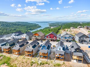 Un barrio residencial con casas, algunas con balcones, y una vista de un lago y colinas al fondo.
