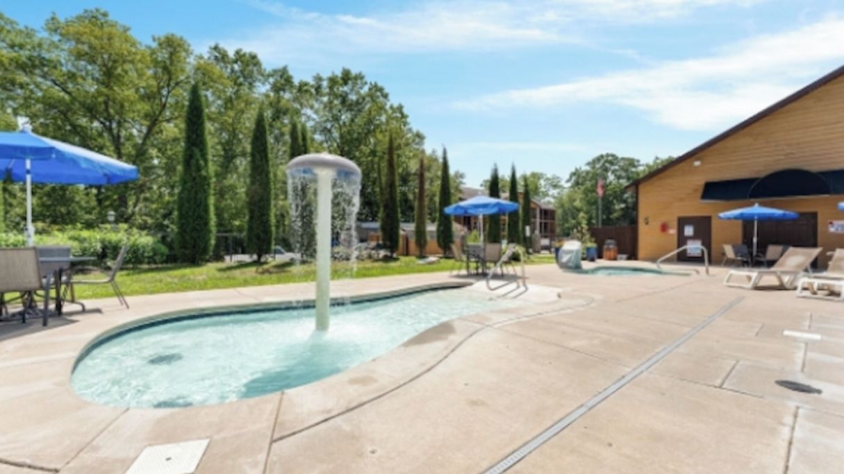 A swimming pool with lounge chairs and umbrellas, surrounded by trees and a building.