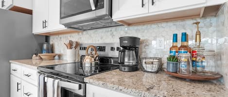 Una cocina moderna con armarios blancos, microondas, cafetera y diversos utensilios de cocina.